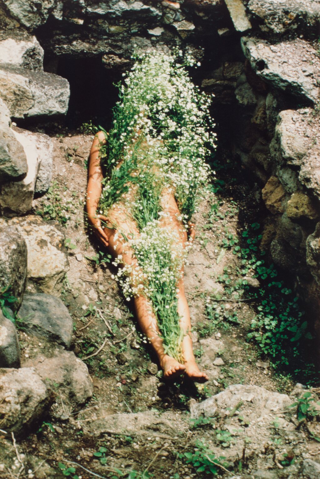Ana Mendieta deitada em uma tumba de Yagul, com o corpo coberto por flores brancas em Imagen de Yagul, da série Silueta.