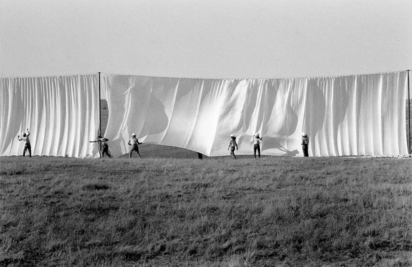 Trabalhadores instalam os grandes painéis de tecido branco de Running Fence em um campo.