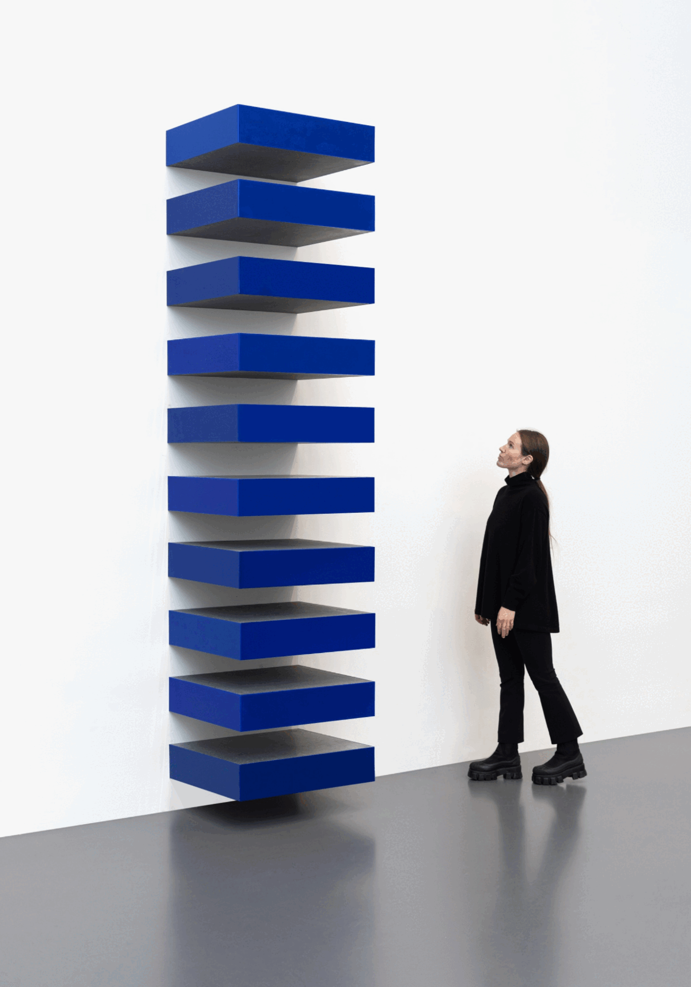Uma visitante observa uma Stack azul de Donald Judd instalada verticalmente numa parede branca.
