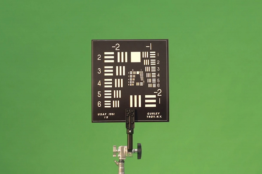 Fotograma de How Not to Be Seen, de Hito Steyerl: um quadro de teste de resolução está montado diante de um fundo verde de chroma key.