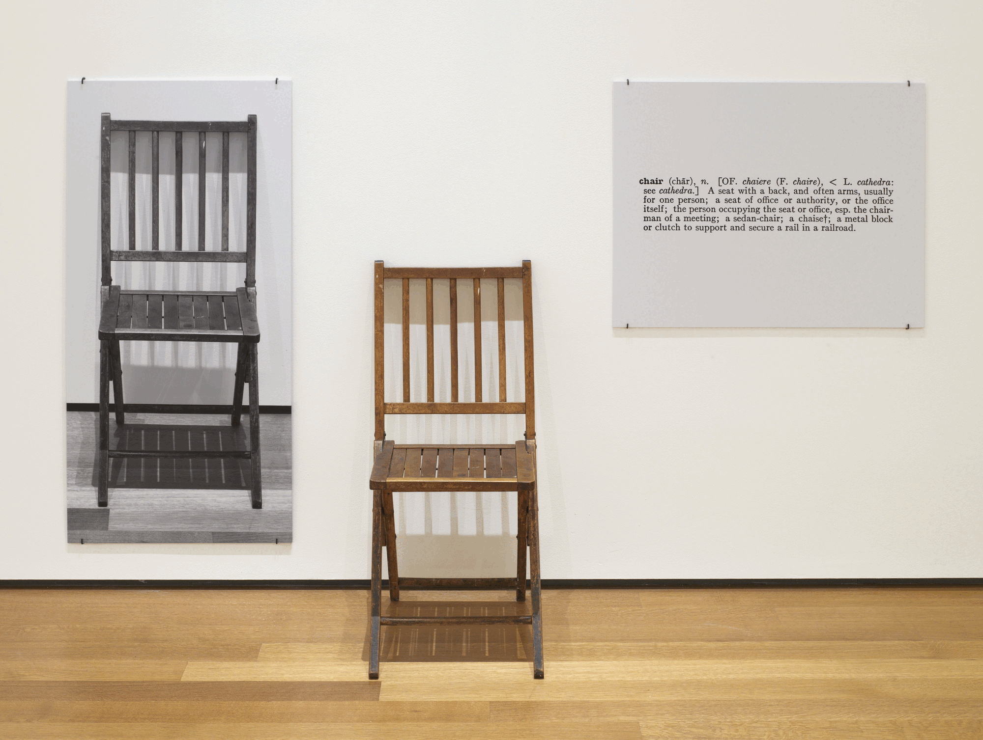 One and Three Chairs, de Joseph Kosuth: uma cadeira de madeira instalada entre sua fotografia em preto e branco e a ampliação da definição da palavra chair.