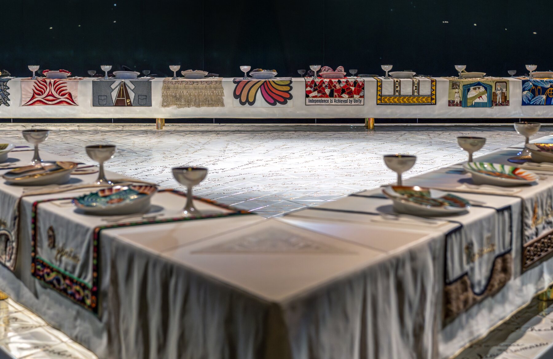 Vista da mesa triangular de The Dinner Party, com pratos, cálices e caminhos de mesa dedicados a mulheres da história.