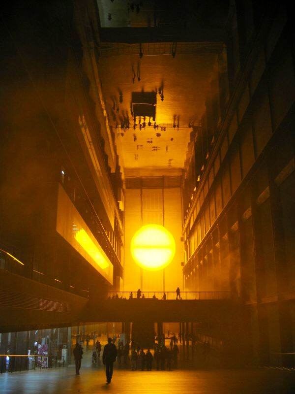 Vista distante da Turbine Hall com o sol artificial de The Weather Project e visitantes refletidos no teto.