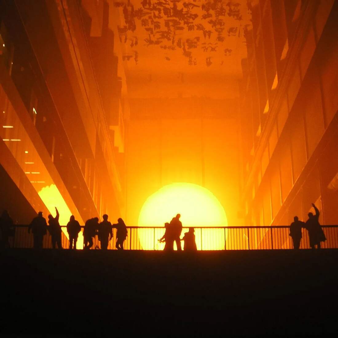 Visitantes observam o sol artificial de The Weather Project enquanto seus corpos aparecem refletidos no teto.